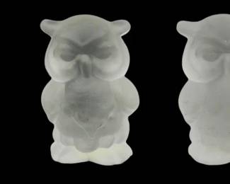 1257 - 4 Frosted Glass Mini Owl Figures (Description): A collection of four frosted glass owl  figures. The set includes three similar  standing owls with closed eyes in a  contemplative pose, and one owl perched on a  branch with open eyes. Each piece displays the characteristic satin-like translucent  finish of frosted glass, creating a soft,  ethereal appearance.
