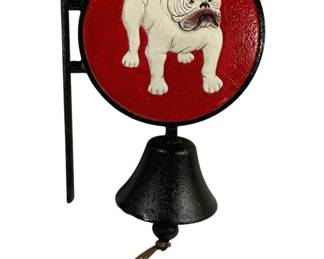 1524 - Cast Iron Bulldog Bell 14"x10"x5.5" (Description): Cast iron wall-mounted bell featuring a  painted bulldog motif. The circular plaque  displays a white English bulldog against a  red background, with a black iron bell  suspended below. Includes a leather pull cord for ringing. Measures 14 inches by 10inches  by 5.5 inches.