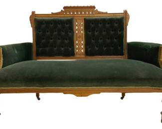 7708 - Victorian Eastlake Green Velvet Settee (Description): Victorian Eastlake style settee featuring a  carved oak frame with pierced fretwork  details on the back and crest rail.  Upholstered in deep green velvet with  button-tufted back panels. The frame displays characteristic Eastlake incised decorative  elements throughout. Rests on turned front  legs with casters. Measures 40 inches high by  59 inches wide by 29 inches deep.