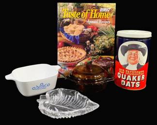 2007 - Assorted Kitchenware Lot w/ Cookbook (Description): A lot of assorted kitchenware and glass items  including a Corning Ware Cornflower pattern  casserole dish, an amber glass covered dish,  a clear pressed glass leaf-shaped dish, a  vintage Quaker Oats advertising tin, and a 1997 Taste of Home Annual Recipes cookbook.