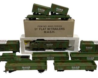 1660 - 9pc MASH 4077th HO Train Set (Description): A 9-piece MASH 4077th HO scale train set  featuring military-themed rolling stock. The  set includes a camouflage diesel locomotive,  various freight cars, gondolas, and a flatcar  with trailers, all decorated in olive drab and camouflage livery with MASH 4077th and US  Army markings. One car retains its original  box labeled '51' Flat W/Trailers M.A.S.H.'  with item number AH43-1039-D4.