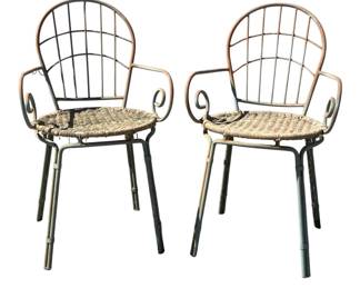 7693 - Pr of Metal Outdoor Chairs w/ Woven Seats (Description): Pair of outdoor chairs featuring painted  metal frames with scrolled armrests and  grid-pattern backs. The seats are woven in a  natural fiber material. The chairs show a  weathered patina consistent with outdoor use, with the metal exhibiting an aged cream and  green finish. Measures 34 inches high by 19  inches wide by 20 inches deep.