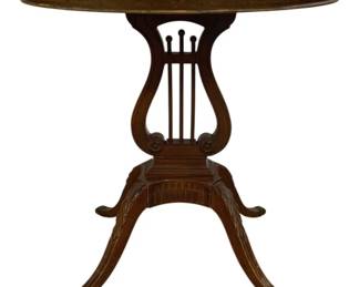 7712 - Mersman Oval Mahogany Oval Lyre Base Table (Description): Oval side table featuring an elegant  lyre-form pedestal base in a rich mahogany  finish. The table has a gallery-edge top  supported by a decorative lyre support with  carved details and a fluted center column. Four gracefully curved splayed legs with  acanthus leaf carvings terminate in brass  capped feet. Duncan Phyfe style design.  Measures 27 inches high by 29 inches wide by  18 inches deep.