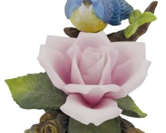 1088 - Andrea by Sadek Porcelain Bluebird Figure (Description): Andrea by Sadek porcelain bird figure  depicting a bluebird perched on a branch  above a delicate pink rose bloom. The figure  features detailed hand-painted plumage in  shades of blue with a yellow breast, accompanied by green leaves and brown  branches. Measures 4.5 inches.