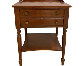 7646 - Sheraton Style Two-Drawer End Table (Description): Sheraton style two-drawer end table in cherry  or mahogany finish. Features a scalloped  gallery top, two drawers with brass ring  pulls, turned and reeded legs, and a lower  shelf. The table exhibits traditional Federal period styling with elegant proportions.  Measures 30 inches high by 21 inches wide by  17 inches deep.