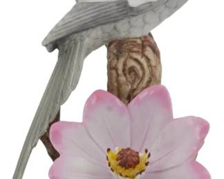 1081 - Andrea by Sadek Porcelain Cockatiel Figure (Description): Andrea by Sadek porcelain cockatiel figurine  featuring a gray and white cockatiel with  distinctive yellow head and orange cheek  patches, perched on a naturalistic brown  branch. The base is adorned with a delicate pink clematis flower and green leaves.  Measures 7 inches tall.