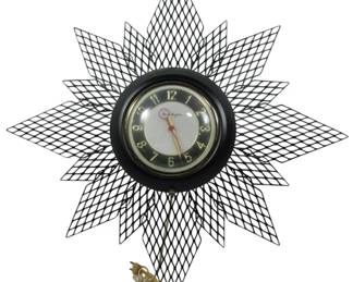 949 - Mid Century Master Crafters Starburst Clock (Description): Mid Century Master Crafters starburst wall  clock featuring a black wire mesh sunburst  design with layered diamond lattice rays. The  central clock face displays Arabic numerals  on a white dial with gold accents and a black inner ring. The electric clock retains its  original power cord. Used as is electric/electronic/mechanical  item. No guarantee all components, untested.