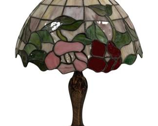 1508 - Tiffany Style Stained Glass Floral Lamp 24" (Description): A Tiffany-style stained glass table lamp  measuring 24 inches tall. The dome shade  features a beautiful floral motif with pink  and deep red flowers surrounded by green  leaves, set against a cream and soft lavender background of leaded glass panels. The shade  has a scalloped edge and is topped with a  decorative finial. The lamp sits on an ornate  cast metal base with an Art Nouveau-inspired  ribbed design and patinated bronze finish.