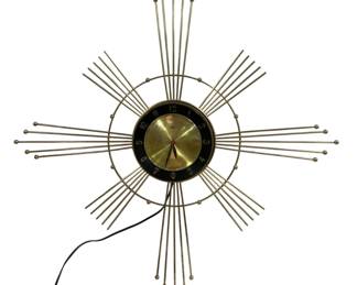 1651 - Starburst Waterford Lux Wall Clock 28" (Description): Waterford Lux wall clock measuring 28 inches.  This mid-century modern starburst style  clock features a gold-tone sunburst design  with radiating metal rods tipped with ball  finials. The clock face has a brass center with a black outer ring displaying Arabic  numerals in silver. Includes original cord  for electric operation. Used as is electric/electronic/mechanical  item. No guarantee all components, untested.