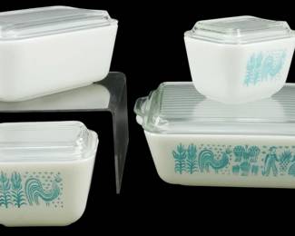 1041 - 4pc Pyrex Butterprint Refrigerator Dish Set (Description): A four-piece Pyrex Butterprint refrigerator  dish set featuring the iconic turquoise on  white Amish pattern with roosters and folk  art motifs. The set includes various sized  rectangular refrigerator dishes, each with clear ribbed glass lids. This beloved  mid-century pattern showcases traditional  Pennsylvania Dutch-inspired imagery including  roosters, corn stalks, and figures in folk  dress.