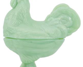 1049 - Jadeite Rooster Covered Jar (Description): The covered dish features a detailed  rooster-shaped lid with finely molded  feathers, comb, and tail plumage, resting  atop a footed base. This collectible piece  showcases the distinctive soft green color characteristic of jadeite glass, popular in  mid-century American kitchenware. Measures 9"  x 7" x 4.5".