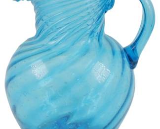 746 - Blue Art Glass Swirl Pitcher 7" (Description): Blue art glass pitcher featuring a swirled  pattern throughout the body and rim. The  piece exhibits hand-blown characteristics  with an applied handle and rounded bulbous  form. Measures 7 inches in height.