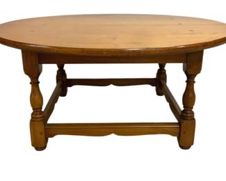 7676 - Lane Pine Coffee Table w/ Turned Legs (Description): A pine coffee table featuring a smooth oval  top with visible wood grain and knots. The  table is supported by four turned legs  connected by a stretcher base with decorative  scalloped apron details. The warm honey-toned finish highlights the natural  character of the wood. Measures 16 inches  tall by 36 inches in diameter.