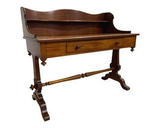 7745 - Antique Mahogany Desk w/ Gallery Back (Description): Antique mahogany desk featuring a shaped  gallery back with curved top rail. The desk  has a single drawer with wooden knob pulls  centered on the front apron. The piece rests  on elegant trestle-style legs with decorative turned finials and a turned stretcher  connecting the two supports. The scrolled  feet and overall construction suggest  Victorian-era craftsmanship. Measures 40" x  46" x 23".