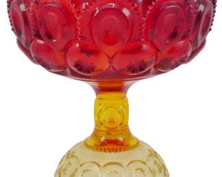 998 - Vtg L.E. Smith Amberina Moon & Stars Compote (Description): Vintage L.E. Smith Amberina Moon & Stars  pattern compote featuring a beautiful  gradient from deep ruby red at the scalloped  rim transitioning to warm amber and pale  yellow at the decorative footed base. The pressed glass design showcases the classic  Moon & Stars motif with circular medallions  and sawtooth detailing throughout. Measures 6  1/2 inches tall by 6 inches in diameter.