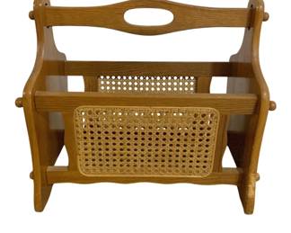 7656 - Oak and Cane Magazine Rack 16"x16"x8" (Description): Oak and cane newspaper or magazine stand  featuring a warm honey-toned wood frame with  cane panel sides. The piece includes a carved  handle cutout at the top for easy  portability, decorative turned wooden finials at the corners, and a sturdy base. This  classic storage piece is ideal for organizing  magazines, newspapers, or other reading  materials. Measures 16 inches by 16 inches by  8 inches.