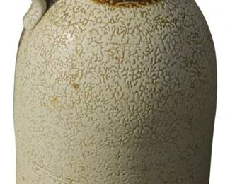 577 - Antique Stoneware Jug w/ Brown Glaze Top 20" (Description): Antique stoneware jug featuring a distinctive  two-tone design with a cream-colored  textured body and dark brown Albany slip  glazed top and handle. The body displays a  characteristic spongeware or salt-glazed texture typical of late 19th to early 20th  century American pottery. The jug has a loop  handle and cork stopper opening. Measures 20  inches tall.