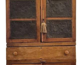 7518 - Rustic Primitive Pie Safe w/ Punched Tins & Key (Description): Antique American pine pie safe featuring six  punched tin panels with decorative floral and  star motifs on the upper cabinet doors. The  piece is constructed with a single drawer at  the waist fitted with wooden knob pulls, and a lower cabinet with two paneled doors. The  case displays characteristic country or  primitive styling with a molded cornice top.  The warm, honey-toned pine shows beautiful  age and patina throughout. Measures 75 inches