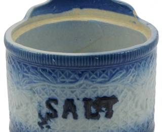 636 - Antique Blue & White Hanging Salt Container (Description): Antique blue and white hanging salt container  featuring decorative embossed patterns and a  pierced hanging tab at the top. The word  "SALT" is prominently displayed on the front.  Measures 7 inches by 6 inches.