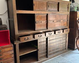 An opened view of the beautiful antique two-section Japanese Mizuya Tansu, a kitchen or tea room chest, with hand forged iron hardware. In two sections, the upper portion has two sets of sliding doors with storage space behind each, and five side-by-side drawers along the lower part. The bottom section has 2 sliding doors with spacious storage with shelving behind. The top cabinet measures 74”W x 20-1/4”D x 39”H and the lower cabinet measures 74”W x 20-1/4”D x 28”H. Likely Meiji Period: (1880-1900). These chests are also known as daidokoro todana (kitchen shelves).