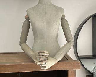 A vintage-style dress form torso with articulated wooden arms and a gray fabric body