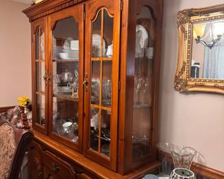 Traditional Wood China Cabinet  Large wood china cabinet featuring glass-paneled upper doors, interior display shelving, and spacious lower cabinets and drawers for additional storage. The warm wood finish and decorative details make it a beautiful statement piece for a dining room or formal living area.