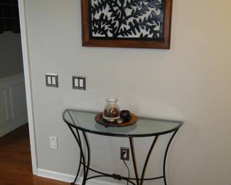 1/2 round glass table with some small decorative items, and nice framed metal art piece