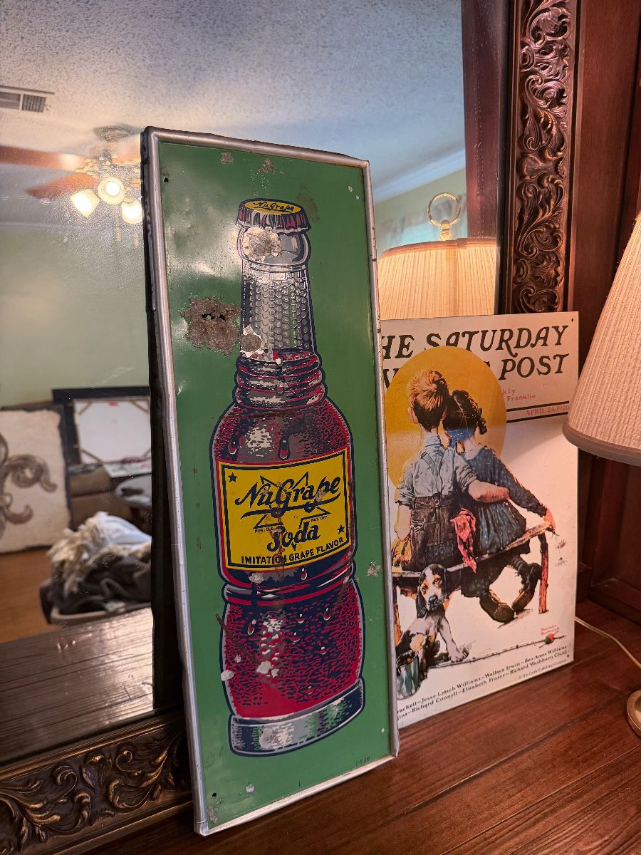 Vintage NuGrape soda metal sign, Saturday Evening Post print, carved wood mirror, and table lamp.