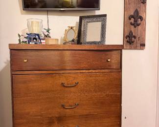 Mid-Century Modern walnut chest of drawers, flat screen TV, table lamps, decorative mirror, glass décor, wall-mounted fleur-de-lis wood plaque, and home décor accents. Great bedroom furniture with vintage MCM style and solid wood storage