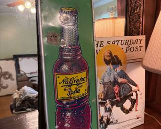 Vintage NuGrape soda metal sign, Saturday Evening Post print, carved wood mirror, and table lamp.