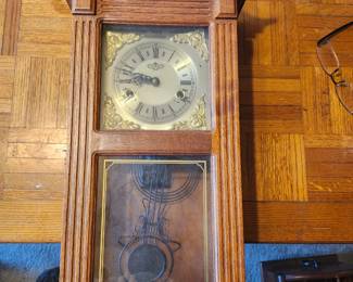 Vintage Oak Pendulum Wall Clock – Key Wind Chime Clock  Beautiful vintage oak wall clock featuring a decorative carved case, brass-tone dial with Roman numerals, beveled glass door, and visible pendulum. This traditional key-wind clock includes both time and strike movements, making it an elegant addition to any home, office, or clock collection.  Crafted in a classic regulator style, this timeless clock offers both functional timekeeping and decorative appeal.  Features:  Solid oak cabinet Key-wind mechanical movement Time and strike function Brass-tone dial with Roman numerals Glass viewing door with decorative pendulum Ready to hang  Manufacturer: Unknown (maker not visible)  Approximate Year: 1970s–1990s  Condition: Good vintage condition with normal wear consistent with age. Glass appears intact. Running condition has not been tested. Includes pendulum; key included only if shown or available.  Suggested Estate Sale Value Quick Sale: $75–100  Buyer pays shipping or local pick up