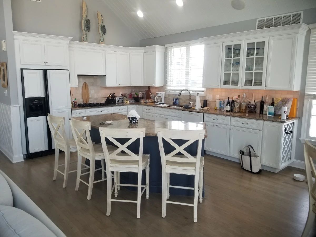 Crisp white kitchen with plenty of upper & lower cabinets; navy island. 4 bar stools by Century Furniture