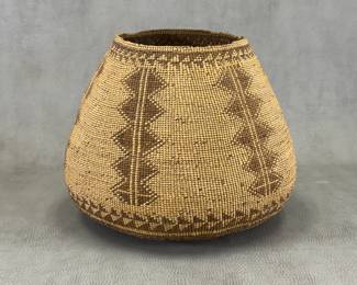 A Native American large, rod-warp twined storage basket with distinctive geometric zigzag pattern woven in contrasting brown and tan fibers; California or Great Basin, tribe undetermined; approximately 8-1/2" tall, base is 10"W and mouth of basket 5-1/2"W.