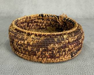 A small handwoven round basket in natural brown fibers with a simple coiled construction
