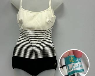 A vintage women's Heinzelman's Orchidee striped colorblock maillot swimsuit – a solid cream or off-white upper bust panel, thin adjustable spaghetti straps, a horizontal black-and-white striped midsection, and a solid black bottom panel with a small gold brand emblem on the left hip. Label has stylized "H" logo and reads "Orchidee Made in West Germany."