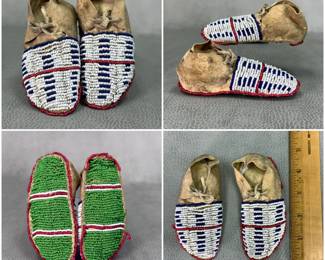 Antique Northern Plains Native American child or baby moccasins with beaded soles. Sinew-sewn hide with upper vamps presenting glass seed beads in dark blue and white striped bars or block patterns with single red lane and red edging; the soles with green beads intersected with white and red lane stitch and with red single bead outline. Integrated leather tie laces through the cuff fold.