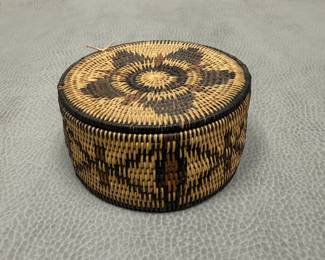 A coiled tightly woven lidded basket with geometric star pattern on lid and diamond/bars design on the sides; approximately 2 inches tall.