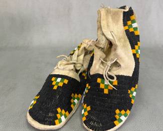 Pair of Native American beaded hide moccasins—likely 19th-century Lakota Sioux or Northern Plains origin—with sinew-sewn tanned hide and intricate beadwork of predominantly black vamp fields accented with distinctive geometric stepped or checkerboard beadwork in black, green, yellow, and white
