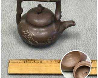 A tiny and traditional Chinese Yixing zisha clay tiliang (over-handle) teapot, featuring an unglazed brown body decorated with delicate incised plum blossom motifs and a branch-form handle, twig-style lid finial; artisan's mark to base and inside of lid