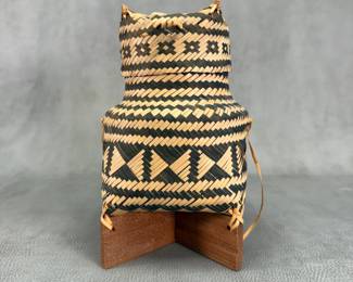 A 19th C. southeast Asian circular basket of plaited black and white rattan, square base, cylindrical neck and cover, its base is fixed to two pieces of wood at right angles; 9 inches tall in total. Per similar example in the British Museum, it’s from the Laos or northern Thailand area, likely made by the Shan or Tai Yuan ethnic groups, and was used to keep cooked sticky rice.