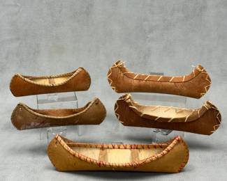 A collection of 5 handcrafted miniature bark canoes, featuring traditional stitched bark hulls and wooden framing details; longest is 12" long and shortest is approximately 9 inches long.