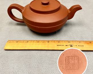 A Chinese Yixing reddish-brown unglazed zisha clay teapot with distinct horizontal ridges wrapping the mid-body, a flat inset lid with a simple round knob, a curved spout, and a looped handle. Maker's mark to base.