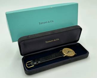 A vintage Tiffany & Co. 14k yellow gold dress wristwatch featuring a round gold-tone case, a textured champagne dial with baton markers, a date window at the 3 o'clock position, and a graphic illustration of the Chicago Tribune Tower, on a black leather strap. In original presentation box, the back of the watch is stamped 14K Tiffany & Co., and inscribed with "To A. Arnam in recognition of the completion of 30 years service 1994 Chicago Tribune.”