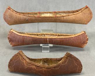 A set of 3 handcrafted miniature birch bark canoes, featuring traditional stitched bark hulls and wooden framing details