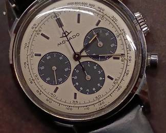 Closeup view of the 1950s-60s vintage Movado M95 "SUB-SEA" Chronograph wrist watch with black leather strap, in the original box. This watch has Movado Factories Swiss in-house Calibre M95 - a 17-jewel, manual-wind, column-wheel chronograph movement developed in partnership with Frédéric Piguet. Case is stainless steel, Fabrique de Boîtiers (FB) / François Borgel. Screw-down caseback stamped with Movado crown, case no. 2496, ref. 95.704.568 with "SUB-SEA" engraved on the case band.