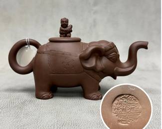 A Chinese Yixing Zisha Clay Elephant Teapot featuring sculpted relief details and a small, seated figure on the lid