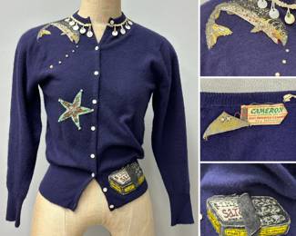 A vintage dark blue/purple knit cashmere cardigan decorated with whimsical aquatic motifs including a leaping rainbow trout trailing small pearl-like beads downwards, a fabric starfish, and a fabric applique can of sardines! Inside labels for Cameron Classics, Inc. cashmere, and Vivienne NY.