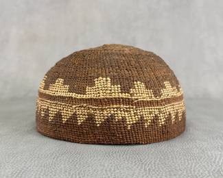 A Native American twined basket hat, possibly Klamath, with fine twining and tight construction typical of Northwest basketry. Brown natural fibers with yellow fiber overlay in geometric pattern band. 7-1/2"W x 4-1/4"H