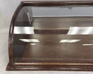 An antique curved glass countertop display case, commonly used in turn-of-the-century general stores, bakeries, and jewelry shops; dark wooden frame and base and single, continuous piece of bent or curved glass that forms the top and front viewing window. 31.5"W x 9.5"H x 16"D