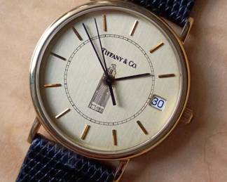 Closeup of the vintage Tiffany & Co. 14k yellow gold dress wristwatch featuring a round gold-tone case, a textured champagne dial with baton markers, a date window at the 3 o'clock position, and a graphic illustration of the Chicago Tribune Tower, on a black leather strap. In original presentation box, the back of the watch is stamped 14K Tiffany & Co., and inscribed with "To A. Arnam in recognition of the completion of 30 years service 1994 Chicago Tribune.”
